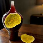 Close-up of a dark glass bottle with yellow sugar crystals around its neck on a wooden table, with a mound of sugar nearby.