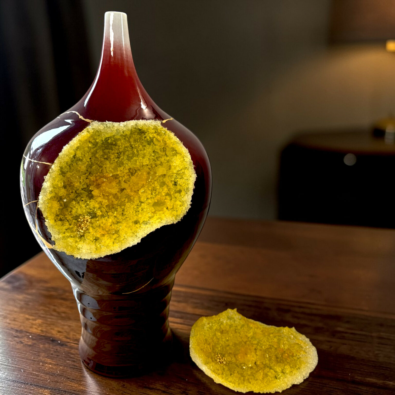 Close-up of a dark glass bottle with yellow sugar crystals around its neck on a wooden table, with a mound of sugar nearby.