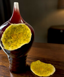 Close-up of a dark glass bottle with yellow sugar crystals around its neck on a wooden table, with a mound of sugar nearby.