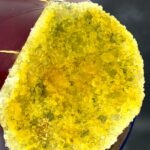Close-up of a red glass bottle with a yellow crystal-geode interior exposed along a cut edge.