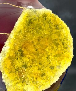 Close-up of a red glass bottle with a yellow crystal-geode interior exposed along a cut edge.