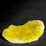 Yellow crystalline mineral fragment resting on a dark surface, sparkling with small crystals