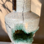 Crackled white ceramic vase with a vertical crack from neck to chest and a small dark brown handle on the side; turquoise crystal glaze decorates a broken opening area.