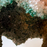 Close-up of a brown rock cavity lined with small turquoise/blue sparkling crystals.