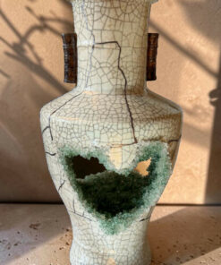 Crackled ceramic vase with two dark brown handles and a large broken opening near the lower body, revealing green crystalline interior.