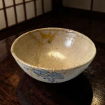 Ceramic bowl with blue decorative patterns and gold repair lines, resting on a dark wooden table.