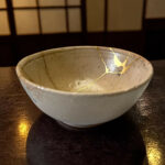 Ceramic bowl with gold kintsugi cracks on a dark wooden table under warm light.