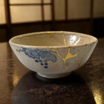 Close-up of a ceramic bowl with blue pattern and gold vein detailing on a dark wooden table surface.