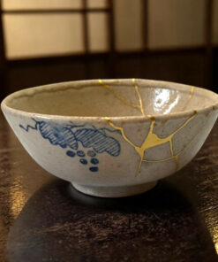 Close-up of a ceramic bowl with blue pattern and gold vein detailing on a dark wooden table surface.