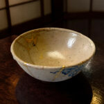 Close-up of a beige ceramic bowl with gold decorative cracks on a dark wooden table.