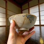 Close-up of a beige ceramic plate tied with gold string, held by a hand against a wooden surface background.