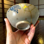 Close-up of a ceramic sphere with blue floral patterns and gold seams being held by hands.