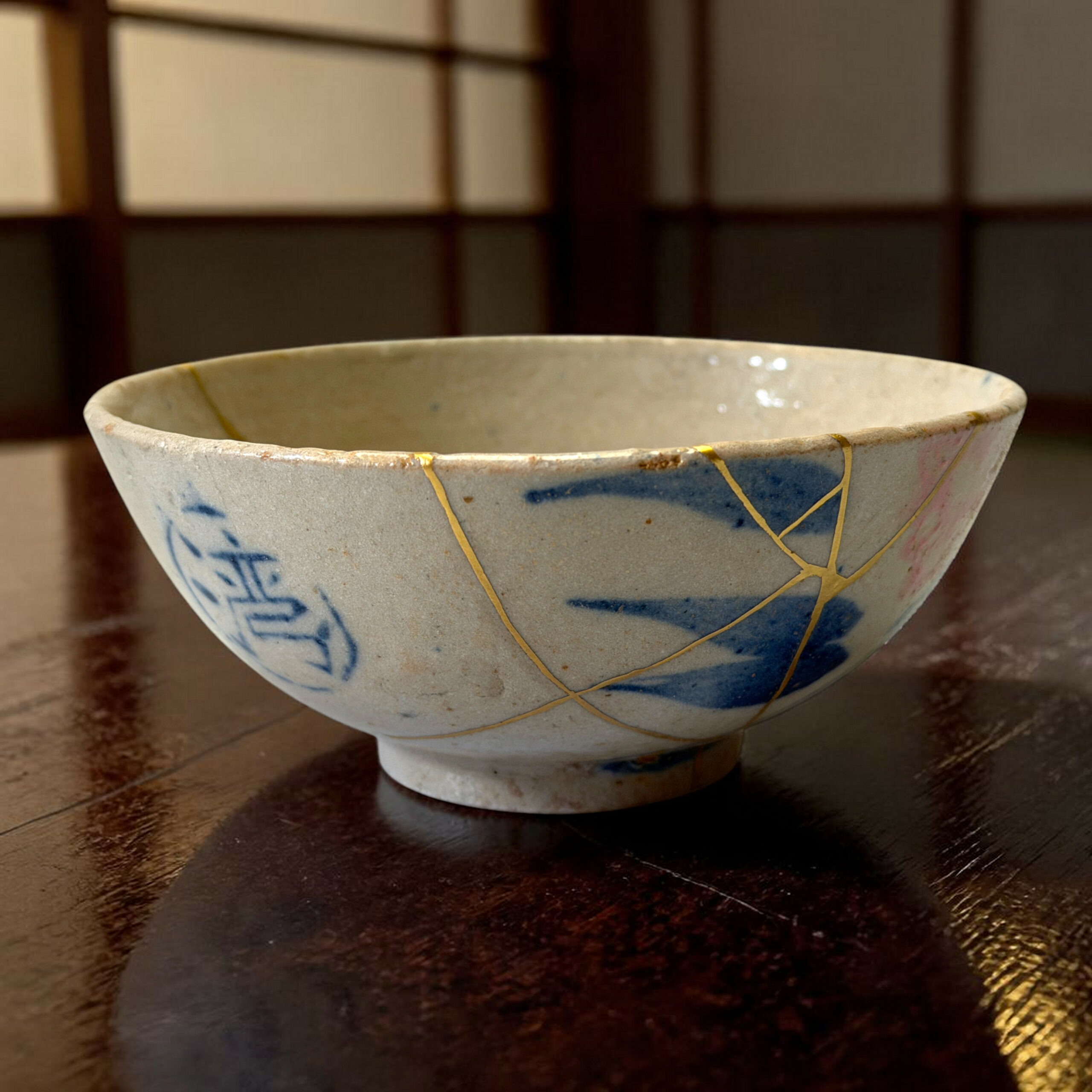 Close-up of a blue-and-white ceramic bowl with gold decorative lines on a dark wooden table.