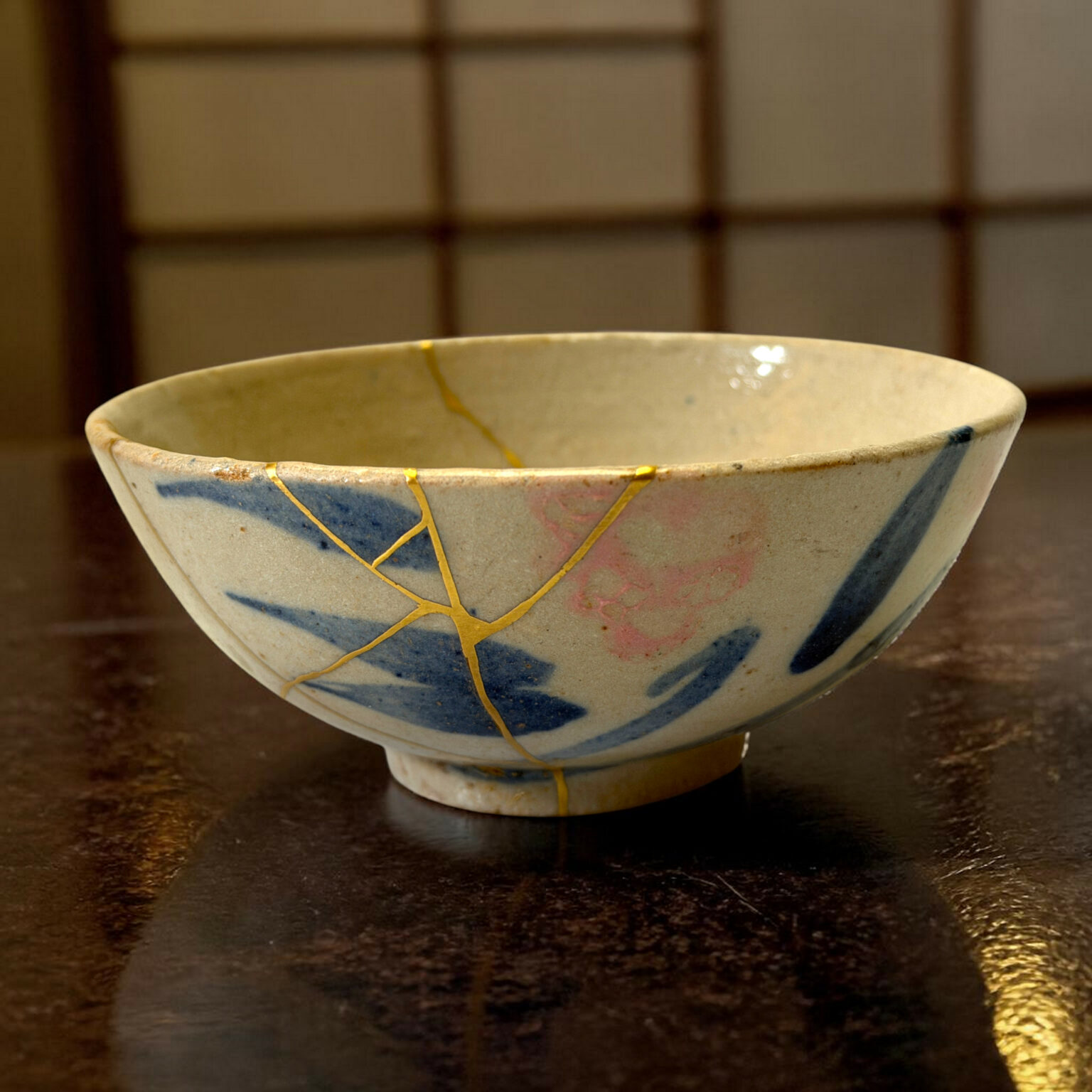 Close-up of a ceramic bowl with blue decorative band and gold crackle lines on a dark wooden table