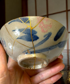 Close-up of a ceramic vase with gold vein patterns being held by hands, a dark wooden background behind it.