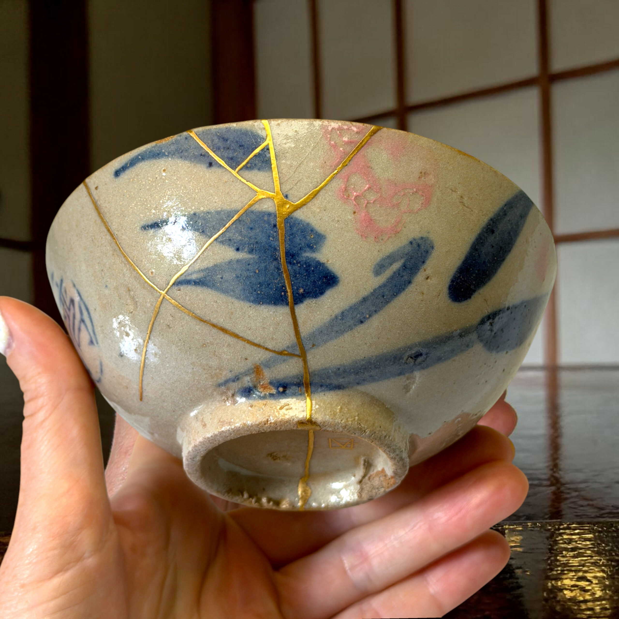 Close-up of a ceramic vase with gold vein patterns being held by hands, a dark wooden background behind it.
