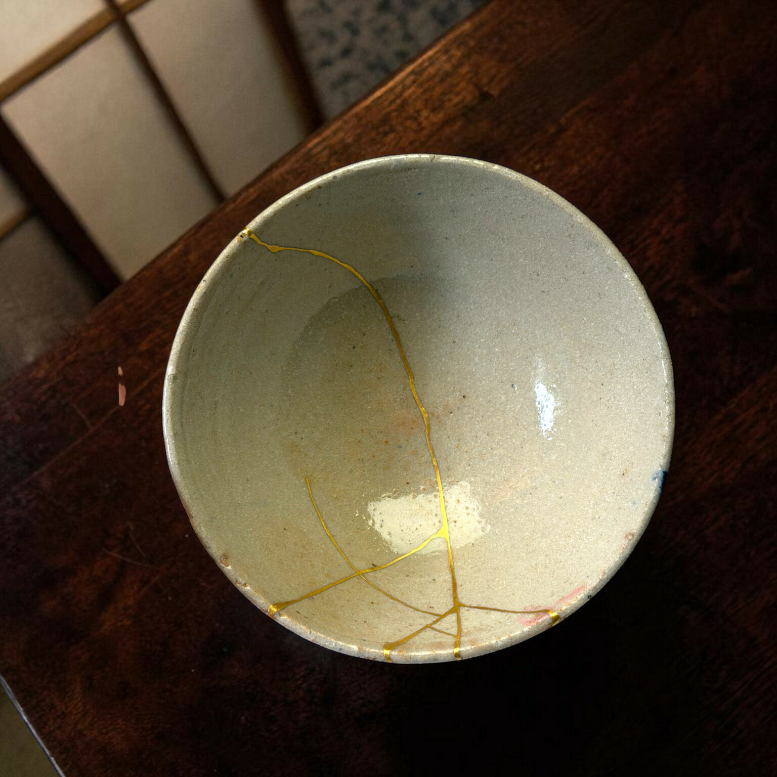 Close-up of a gray ceramic plate with a yellow string wrapped around its rim, resting on a dark wooden surface; small cracks visible on the glaze.