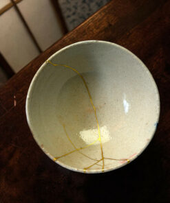 Close-up of a gray ceramic plate with a yellow string wrapped around its rim, resting on a dark wooden surface; small cracks visible on the glaze.