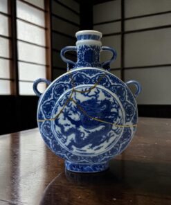 Blue and white porcelain vase with twin handles on a polished wooden table, reflected in the surface.