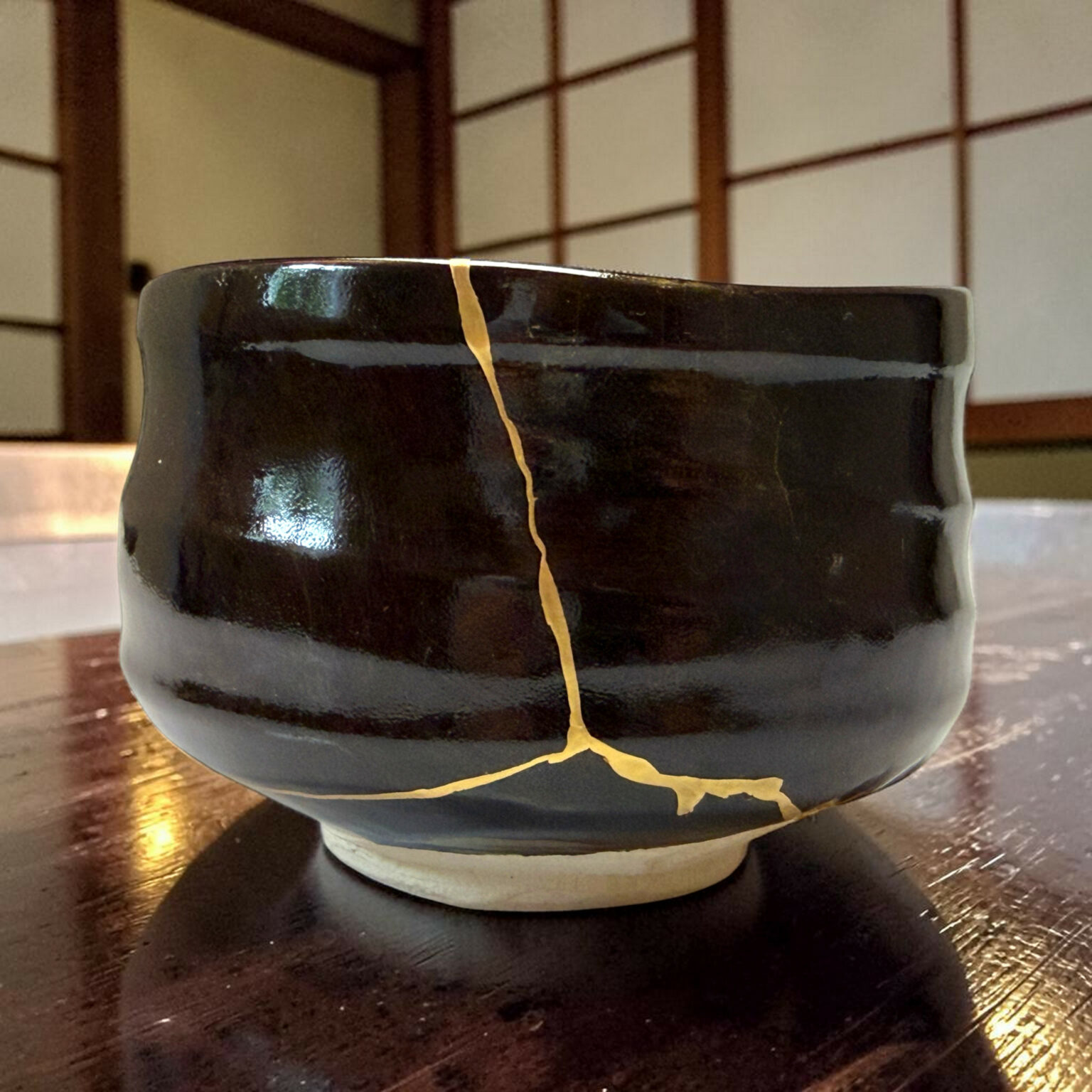 Close-up of a glossy black ceramic mug with a gold crack running vertically down the side, resting on a wooden table.