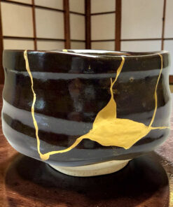 Decorative black ceramic pot with gold vein-like cracks resting on a wooden table, lattice background behind it.