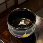 Close-up of a black ceramic pot with gold glaze veining on a wooden table surface.