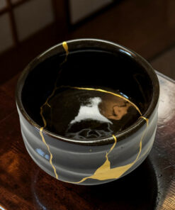 Close-up of a black ceramic pot with gold glaze veining on a wooden table surface.