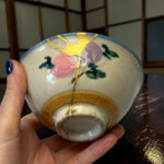 Close-up of a floral-patterned ceramic plate with gold crackle glaze, held by a hand with blue nail polish.