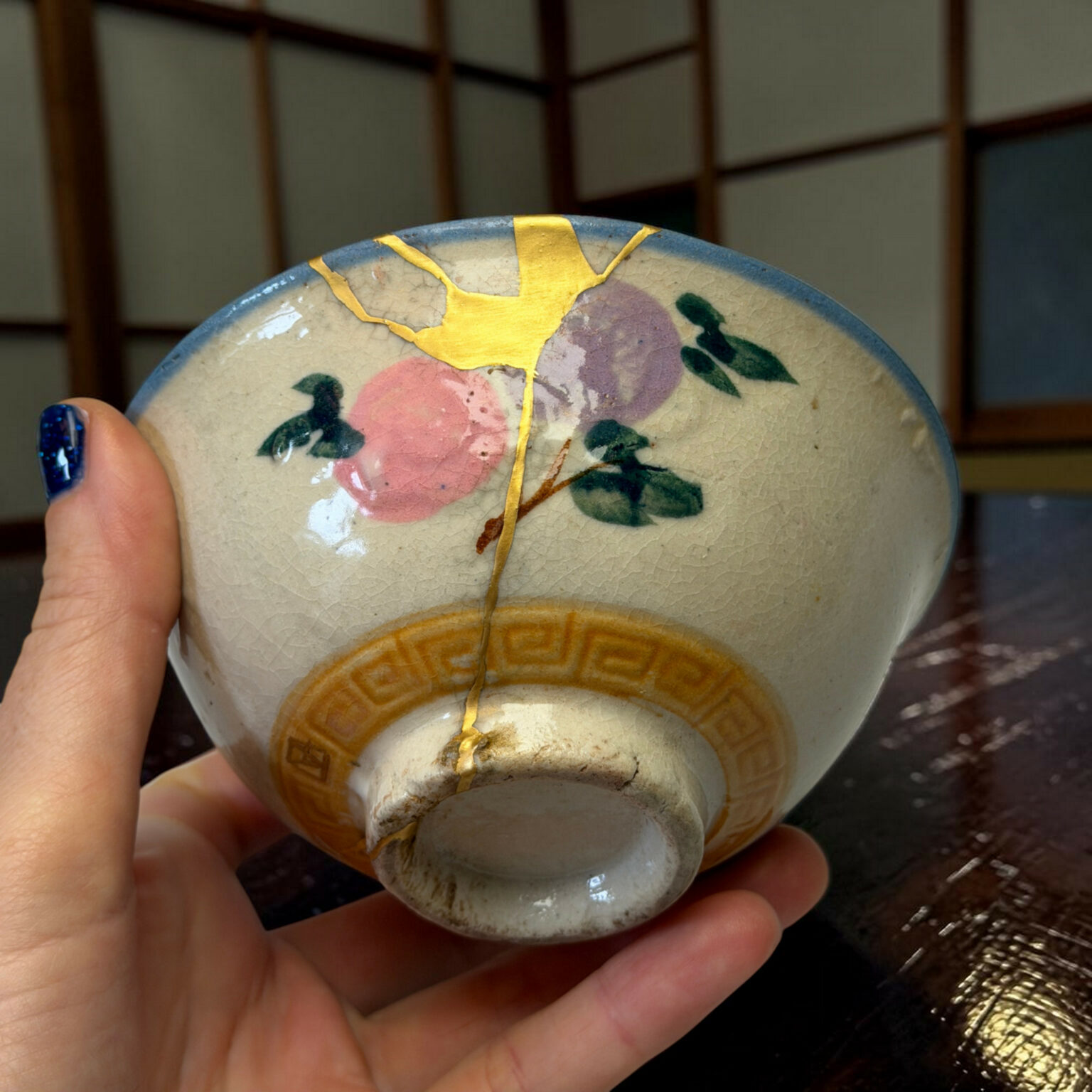 Close-up of a floral-patterned ceramic plate with gold crackle glaze, held by a hand with blue nail polish.