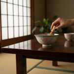 Hand whisking matcha with a bamboo whisk in a ceramic bowl on a wooden table in a traditional Japanese room