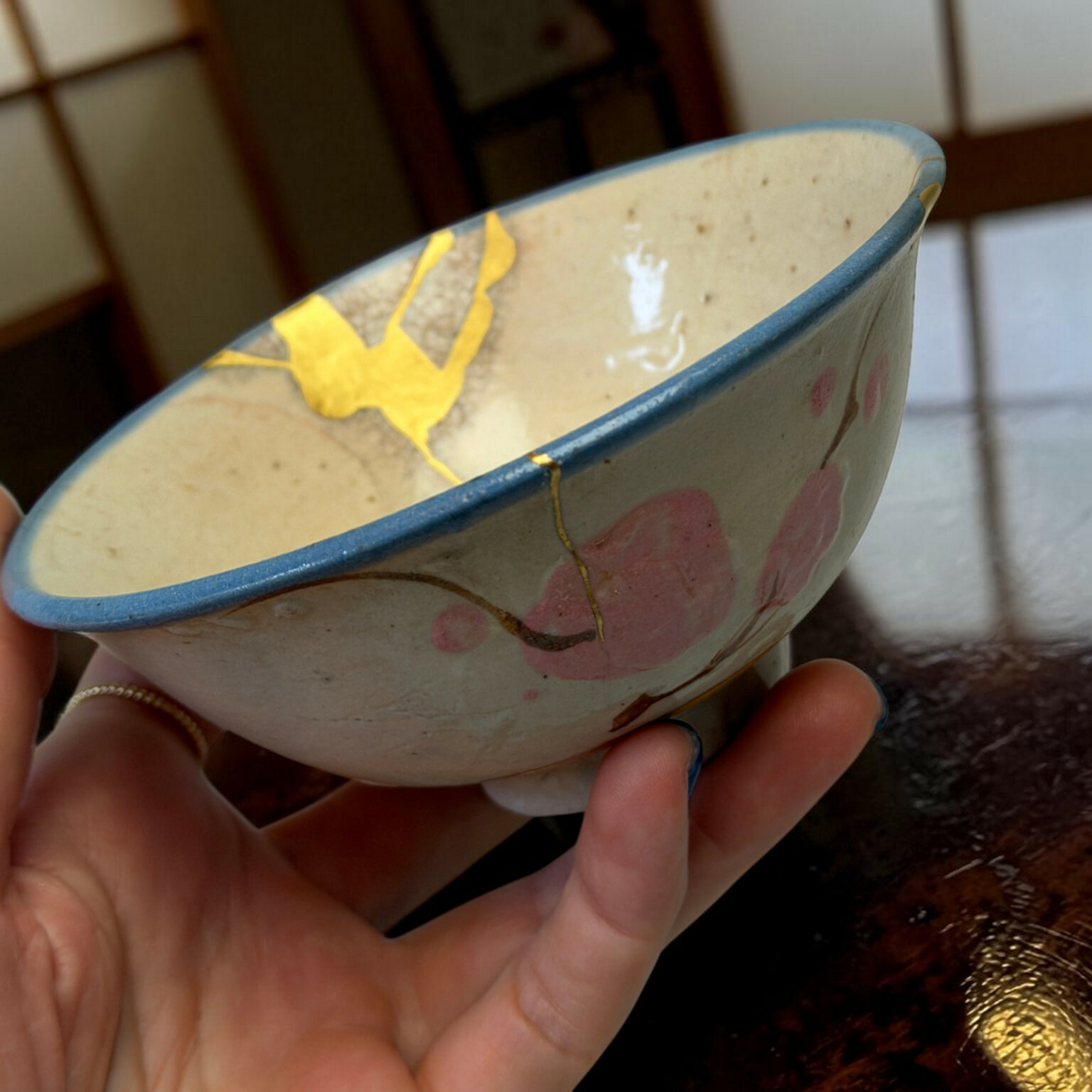 Close-up of a small ceramic bowl with a blue rim, yellow decoration, held in a person's hands.