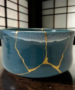 Blue ceramic mug with gold decorative lines sits on a dark wooden table; background features a blurred grid pattern.