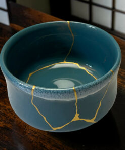 Blue ceramic mug with gold repair lines (kintsugi) running along the rim and interior, placed on a wooden table.