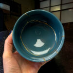 Close-up of a teal ceramic bowl with gold decorative lines held by a hand indoors.