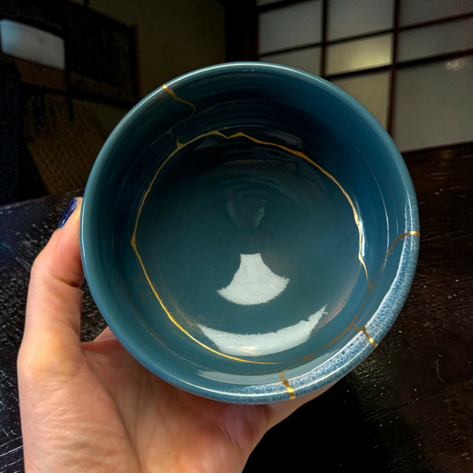 Close-up of a teal ceramic bowl with gold decorative lines held by a hand indoors.