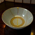 Close-up of a pale blue ceramic plate with gold decorative lines on a dark wooden table left and center-aligned in the frame.