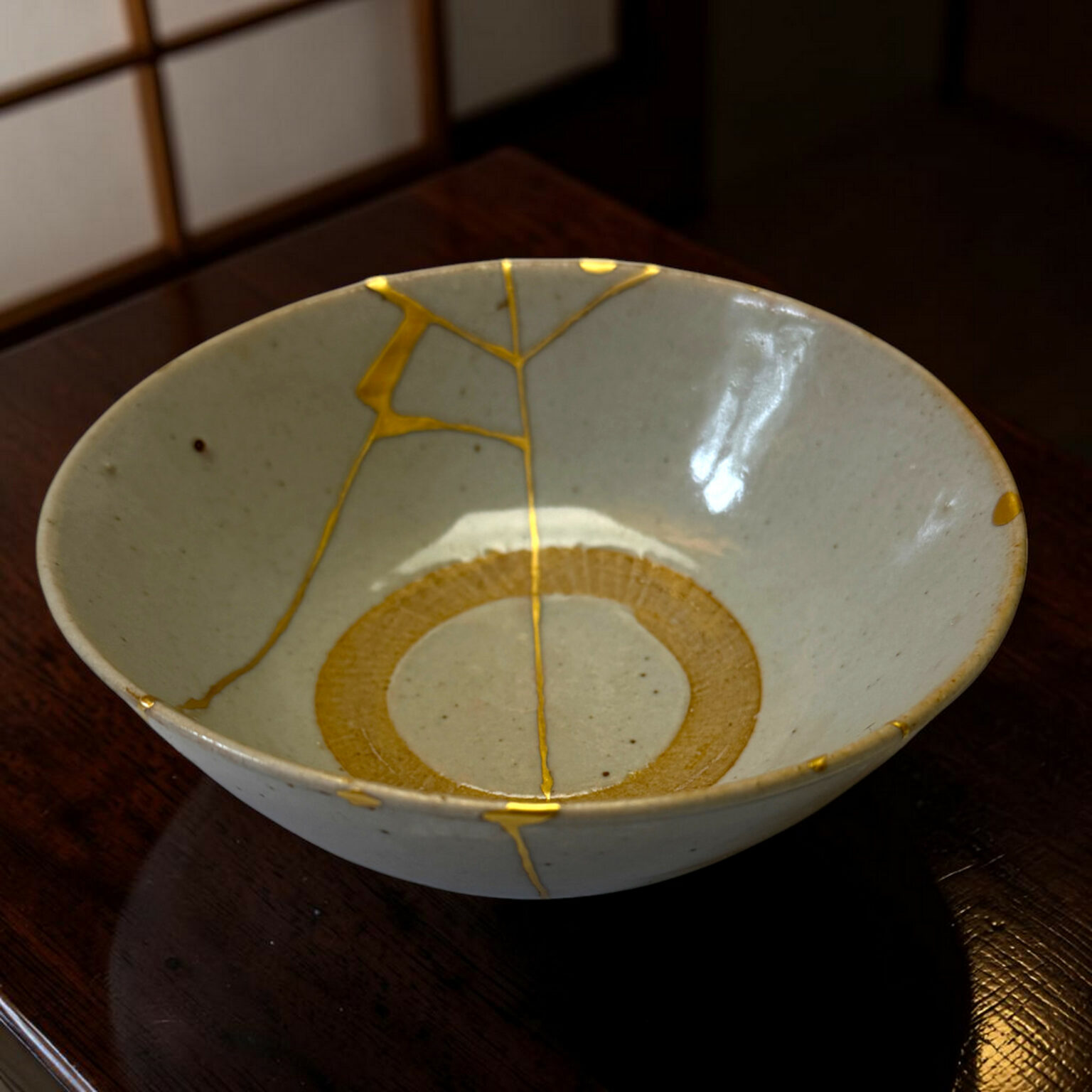 Close-up of a pale ceramic bowl with gold decorative crackle lines on a dark wooden table edge visible at the bottom left.