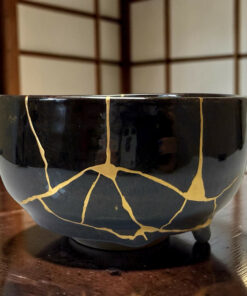 Close-up of a glossy black ceramic mug with a gold crackle pattern, resting on a wooden table.