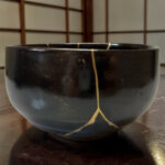 Close-up of a glossy black ceramic bowl rim with a light-colored string draped over it, wooden lattice background blurred.
