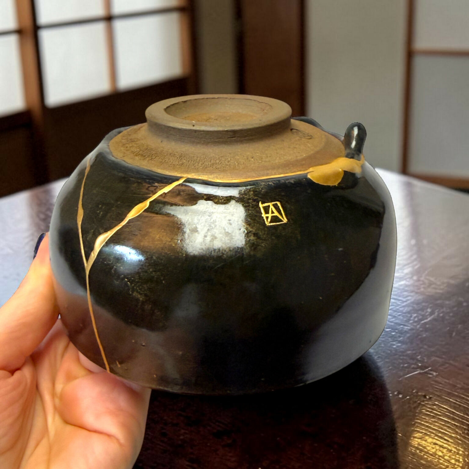 Close-up of a dark ceramic pot with a circular, dusty lid and a yellow string tied around it on a wooden table.