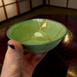 Green ceramic bowl with gold crackle lines being held by a hand over a wooden table.