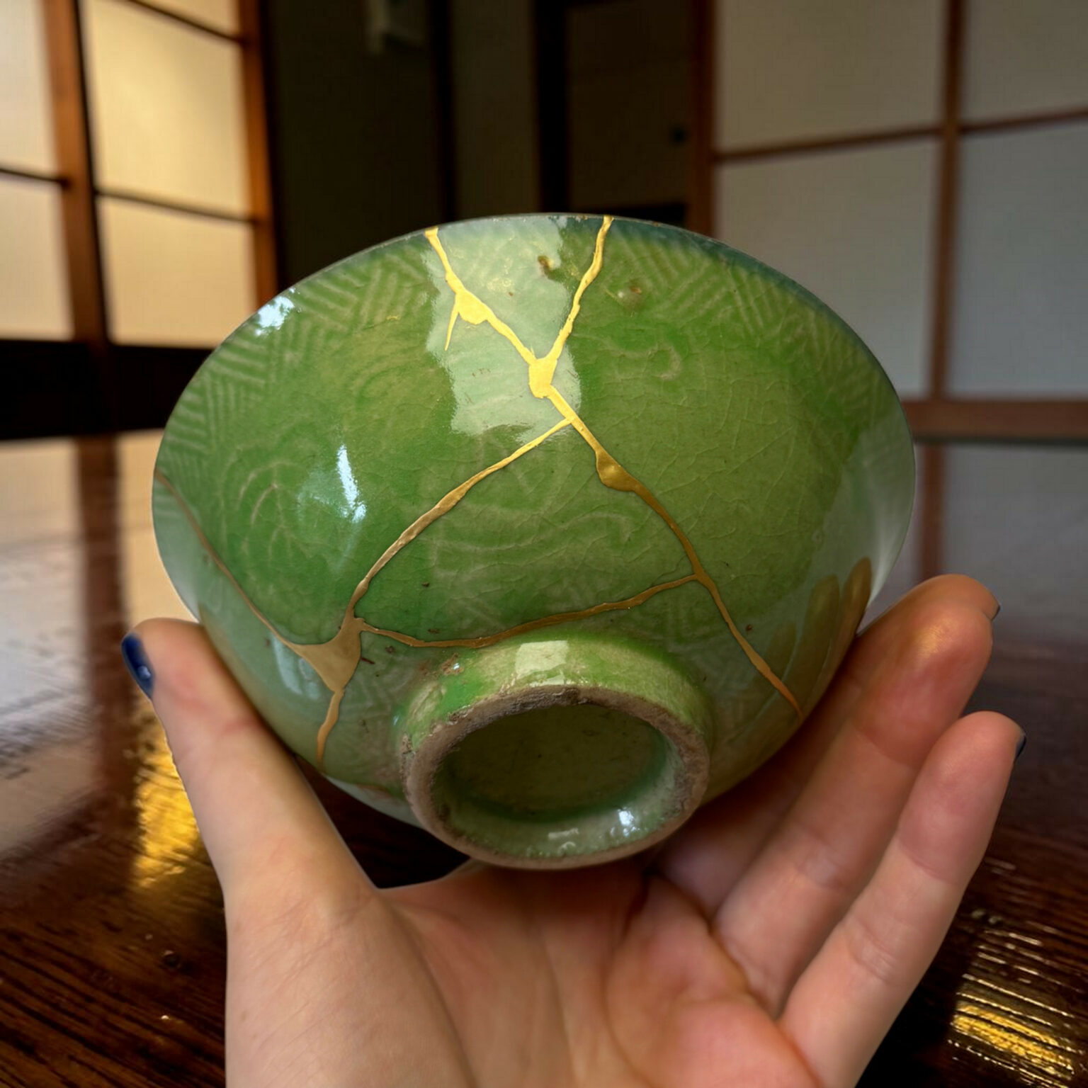 Close-up of a green sphere with gold vein-like cracks being held in both hands over a wooden surface.