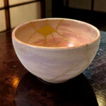 Close-up of a light gray ceramic bowl showing yellow crackle glaze lines inside and along its rim, resting on a dark wooden table in warm lighting.