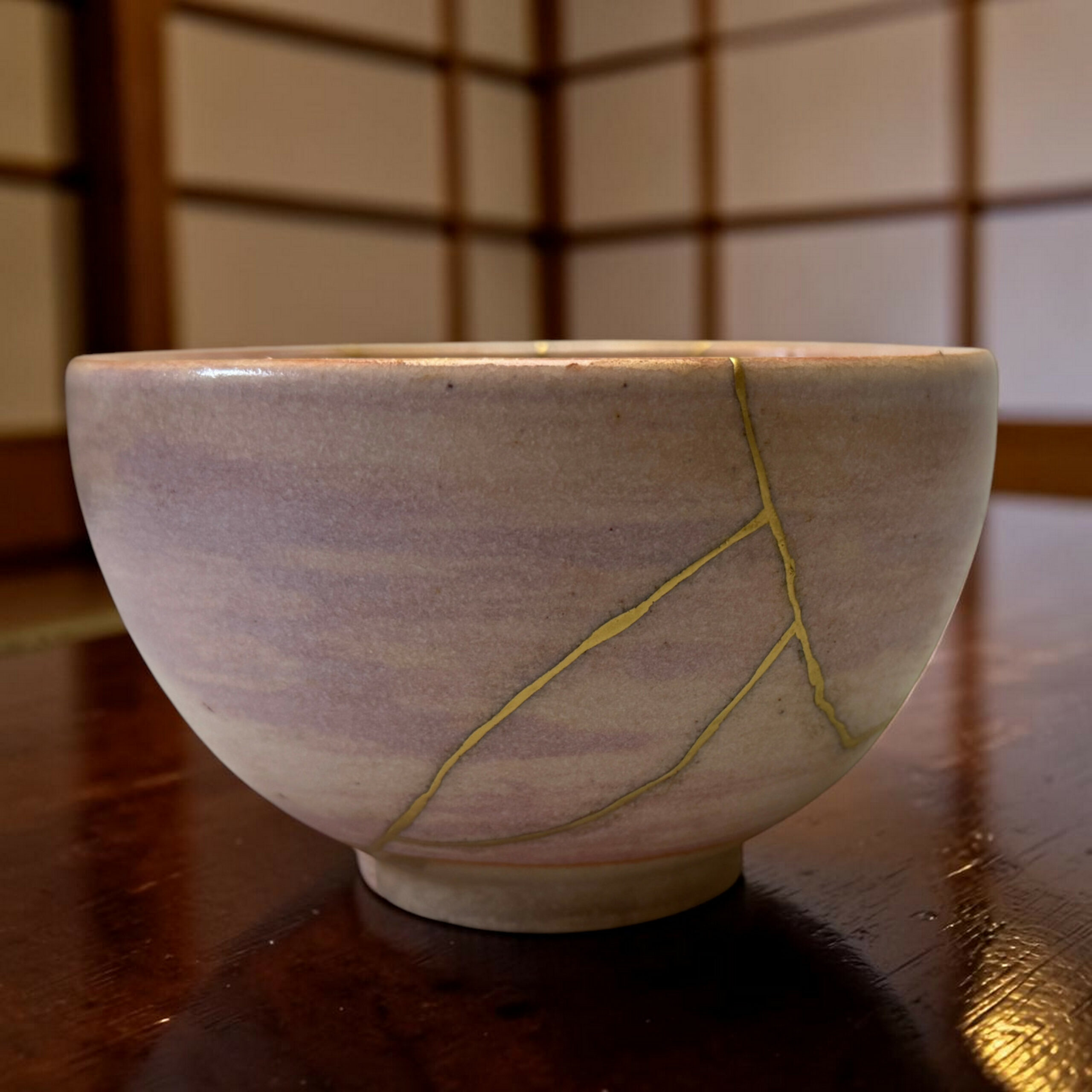 Close-up of a light gray ceramic bowl with a yellow string laid across it, on a dark wooden table (background blurred).