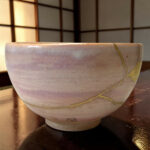 Close-up of a purple-glazed ceramic bowl on a dark wooden table, with a yellow string wrapped around it.