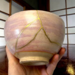 Close-up of a tan rounded sculpture with yellow string stitched in a geometric pattern, held by a hand.
