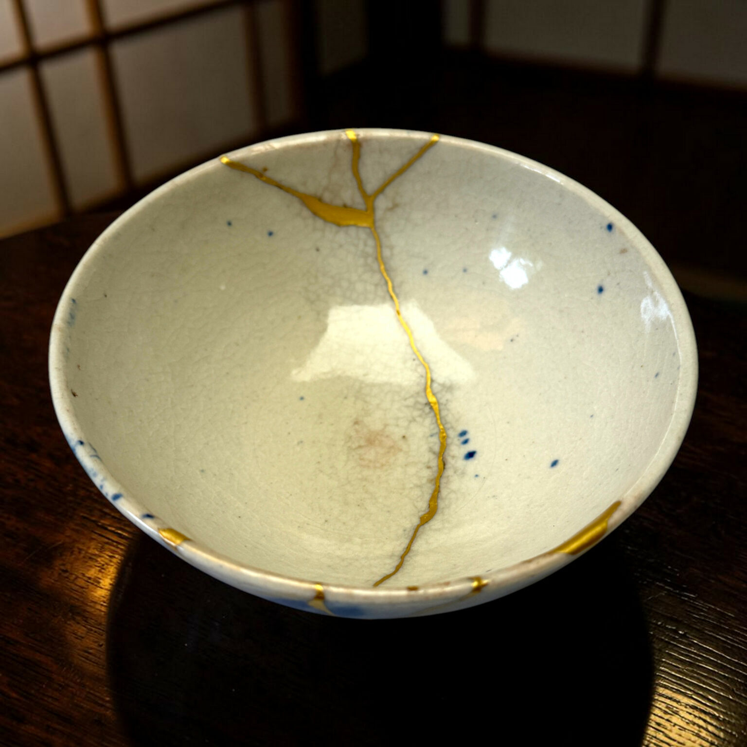 Close-up of a pale ceramic bowl with blue speckles and a yellow glaze line running along the rim, placed on a dark wooden table.