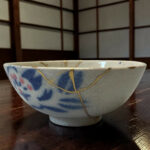 Blue and white ceramic bowl with gold repair stitching resting on a dark wooden table