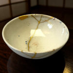 White ceramic bowl with blue speckles and gold crackle glaze along the rim, resting on a dark wooden table.