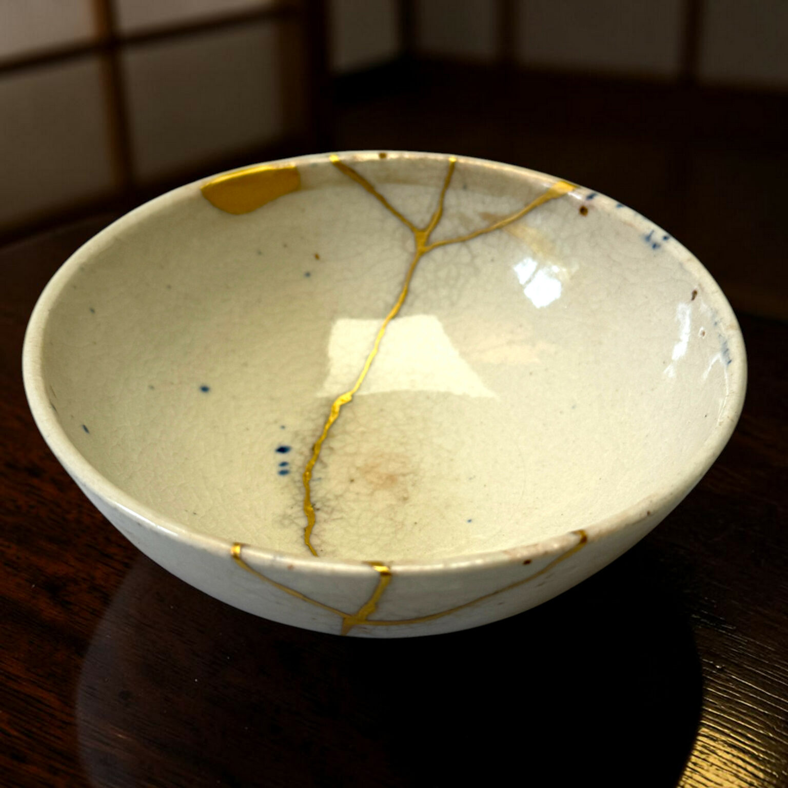 White ceramic bowl with blue speckles and gold crackle glaze along the rim, resting on a dark wooden table.